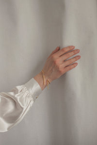 Odkryj delikatną bransoletkę na rękę składającą się z obręczy i dwóch wiszących końcówek, wykonaną ręcznie ze srebra 925 lub pozłacanego 24-karatowym złotem. Model z kolekcji U, inspirowanej minimalizmem, charakteryzującej się prostymi przecinającymi się liniami i geometrycznymi kształtami.